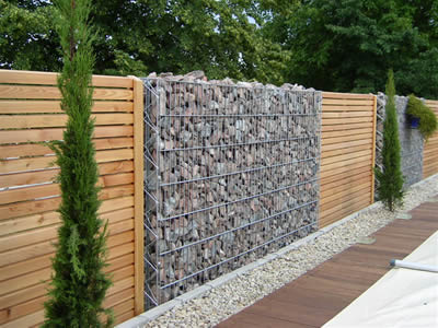 A high stainless steel welded mesh gabion basket between two wooden fences serve as a wall together.